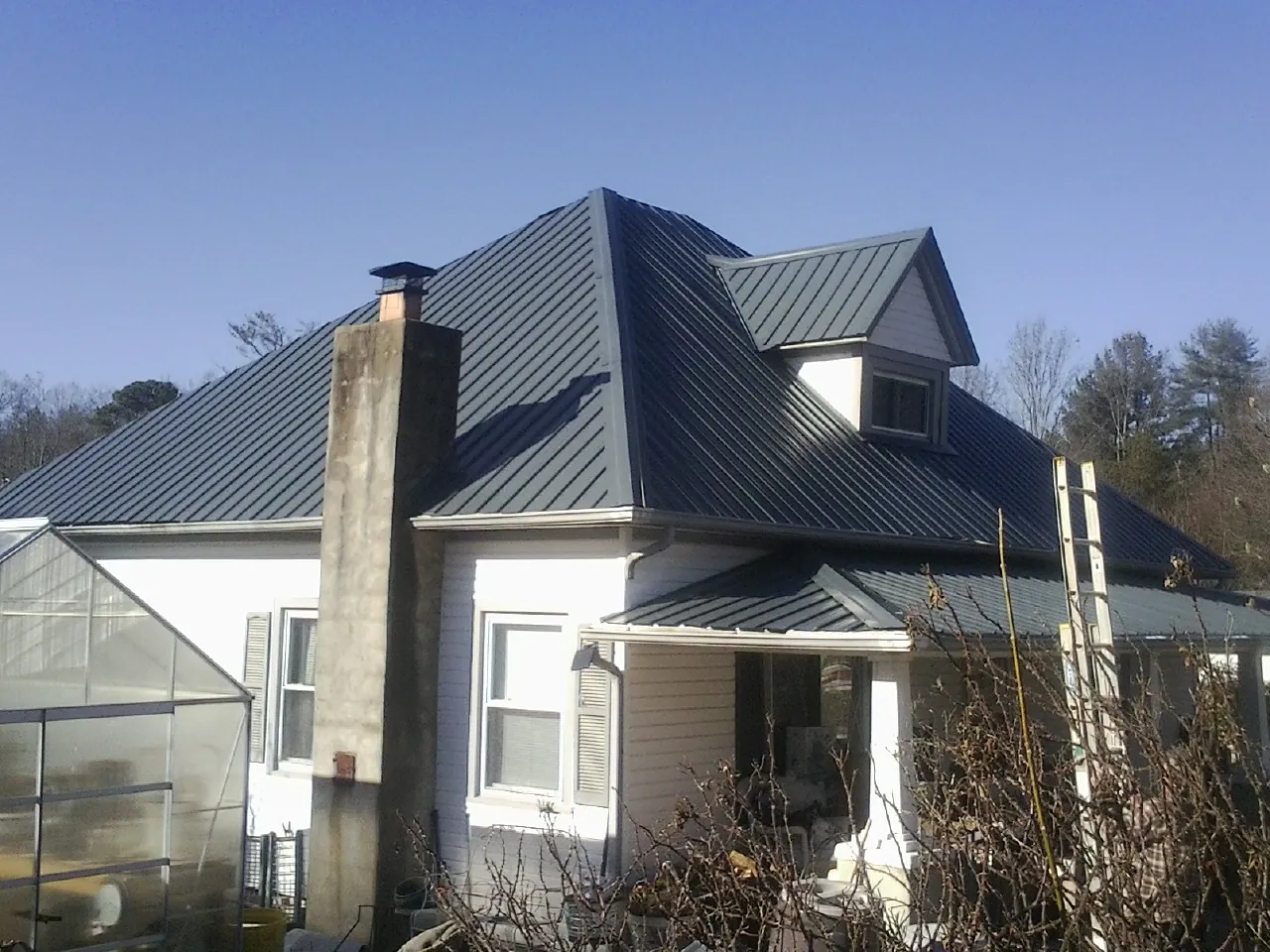 Dark blue standing seam metal roof on a white farmhouse with dormer — Slate & Tile Roof Repair by Roofing Brothers in Buna
