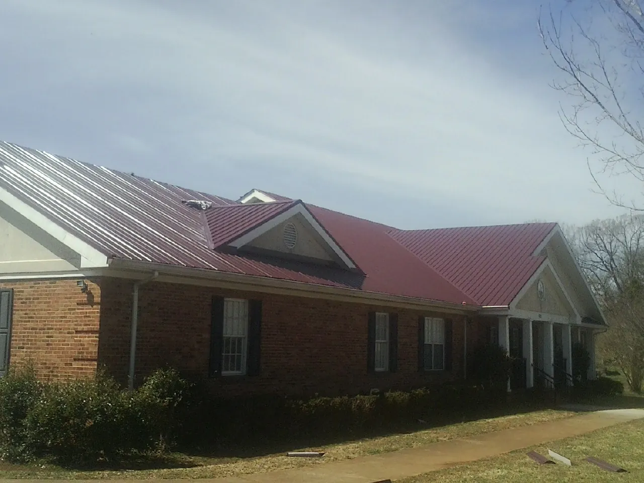 Red metal roof with gabled entries on a long brick building, from a Hail Damage Roof Repair job in Buna
