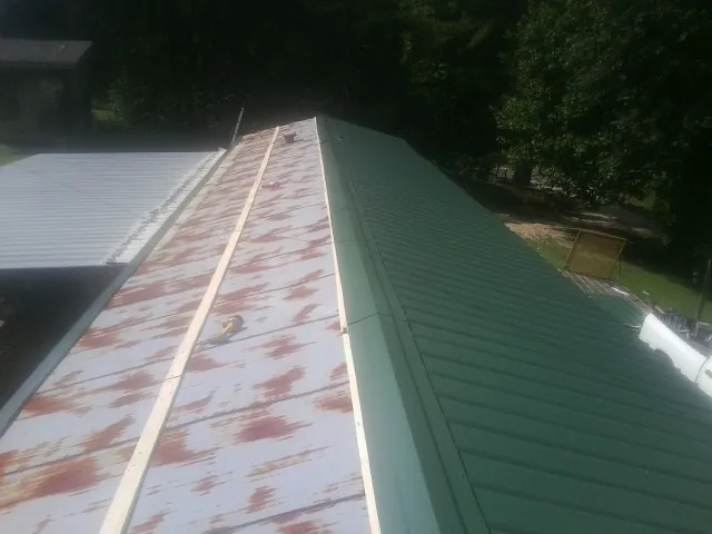 Old rusted panels beside newly installed green metal roofing — Wind Damage Roof Repair by Roofing Brothers in Buna