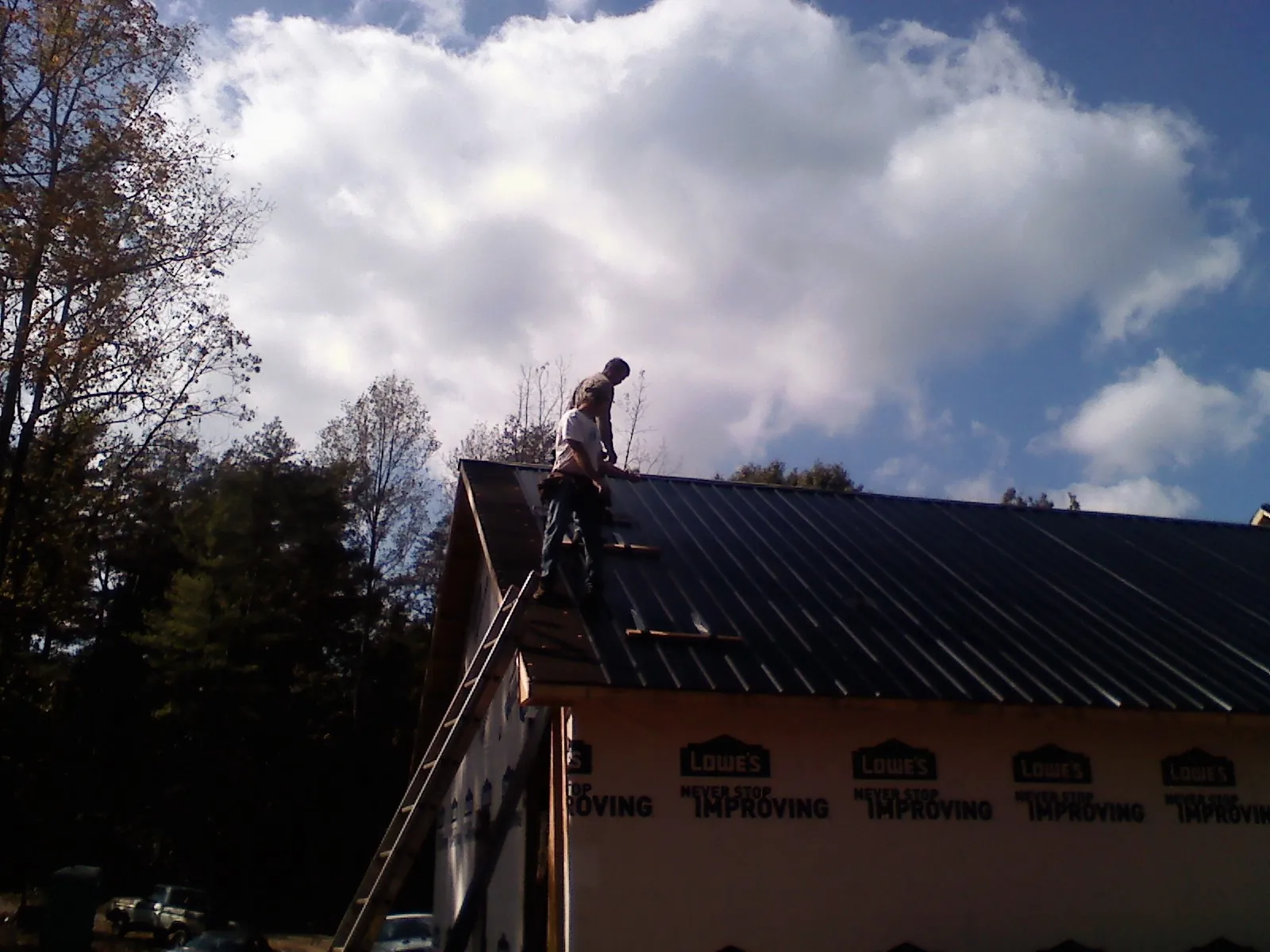 Roofer fastening dark metal panels high against a cloudy sky, from a Roof Inspection job in Buna