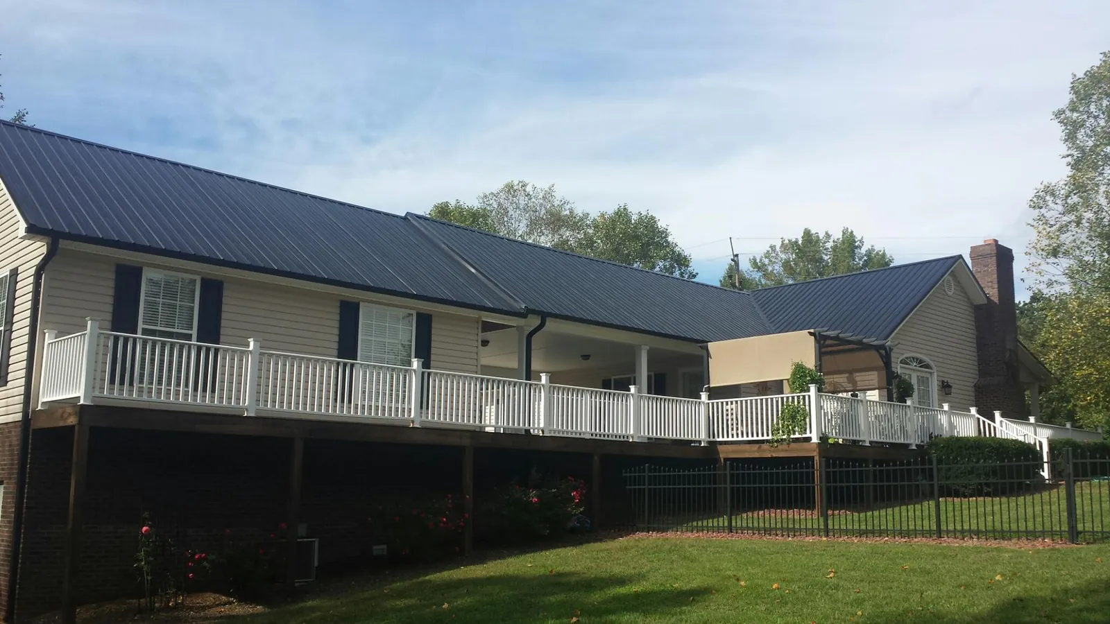 Black metal roof above a long white railed deck on a hillside home in Buna