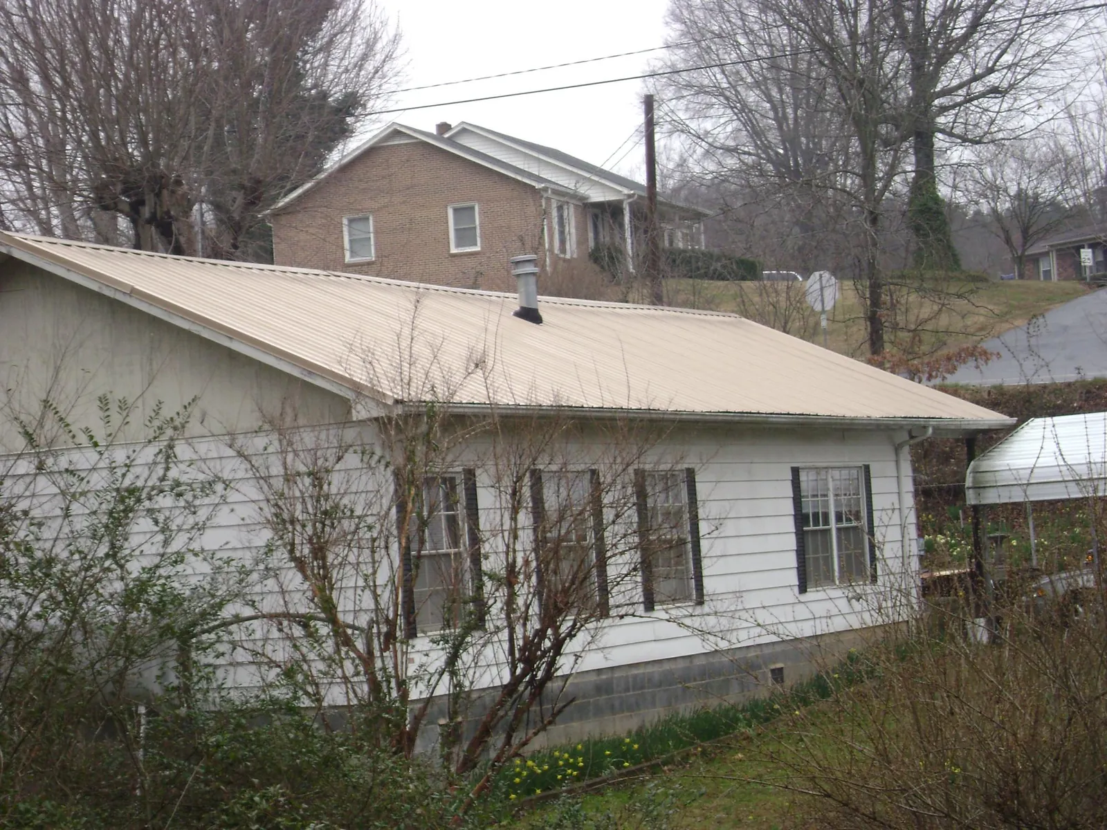 Tan metal roof on a white sided house set into a hillside — Commercial Roofing by Roofing Brothers in Buna