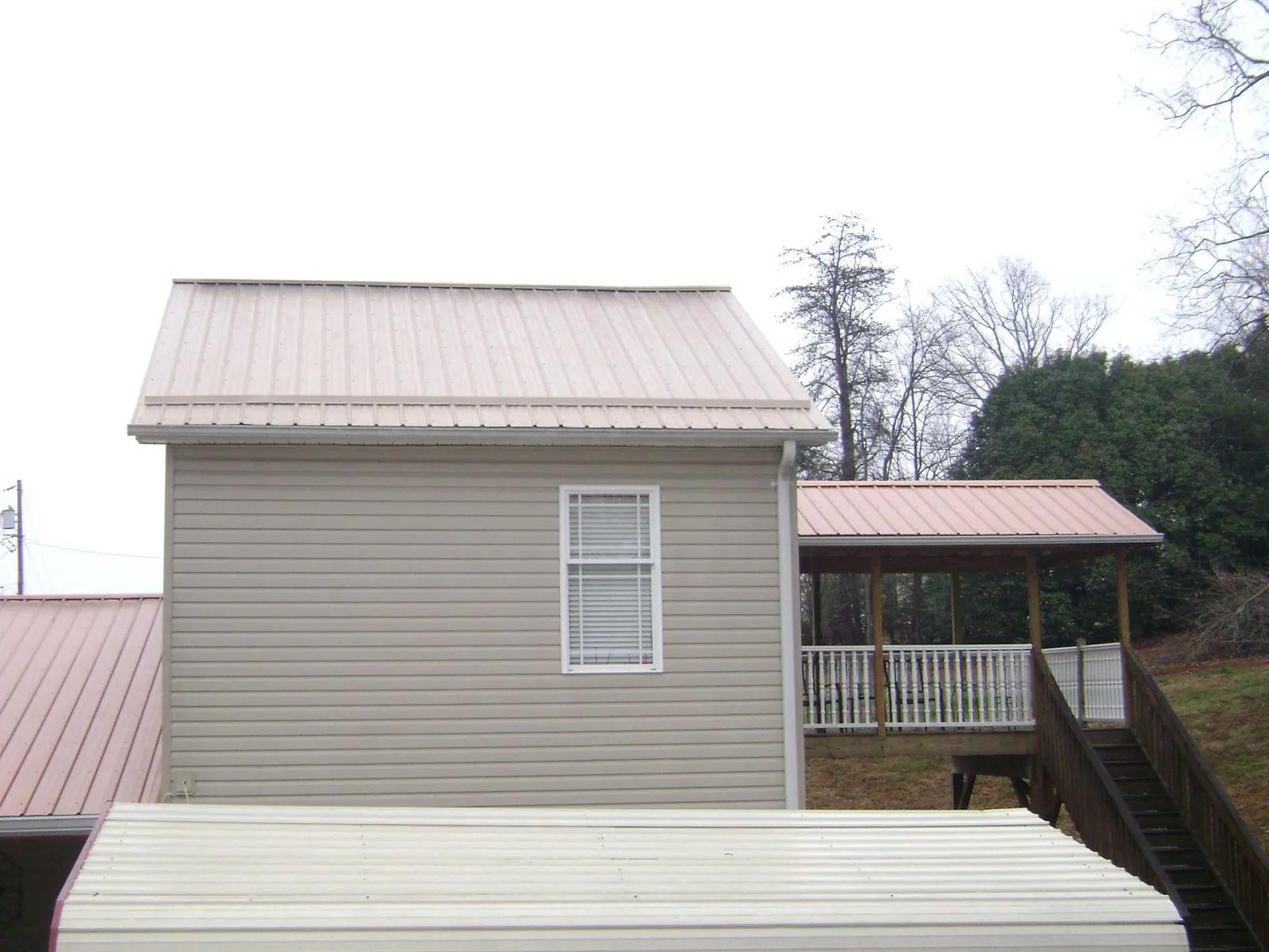 Tan metal roofs on a two story addition and attached porch, from a Roof Replacement job in Buna